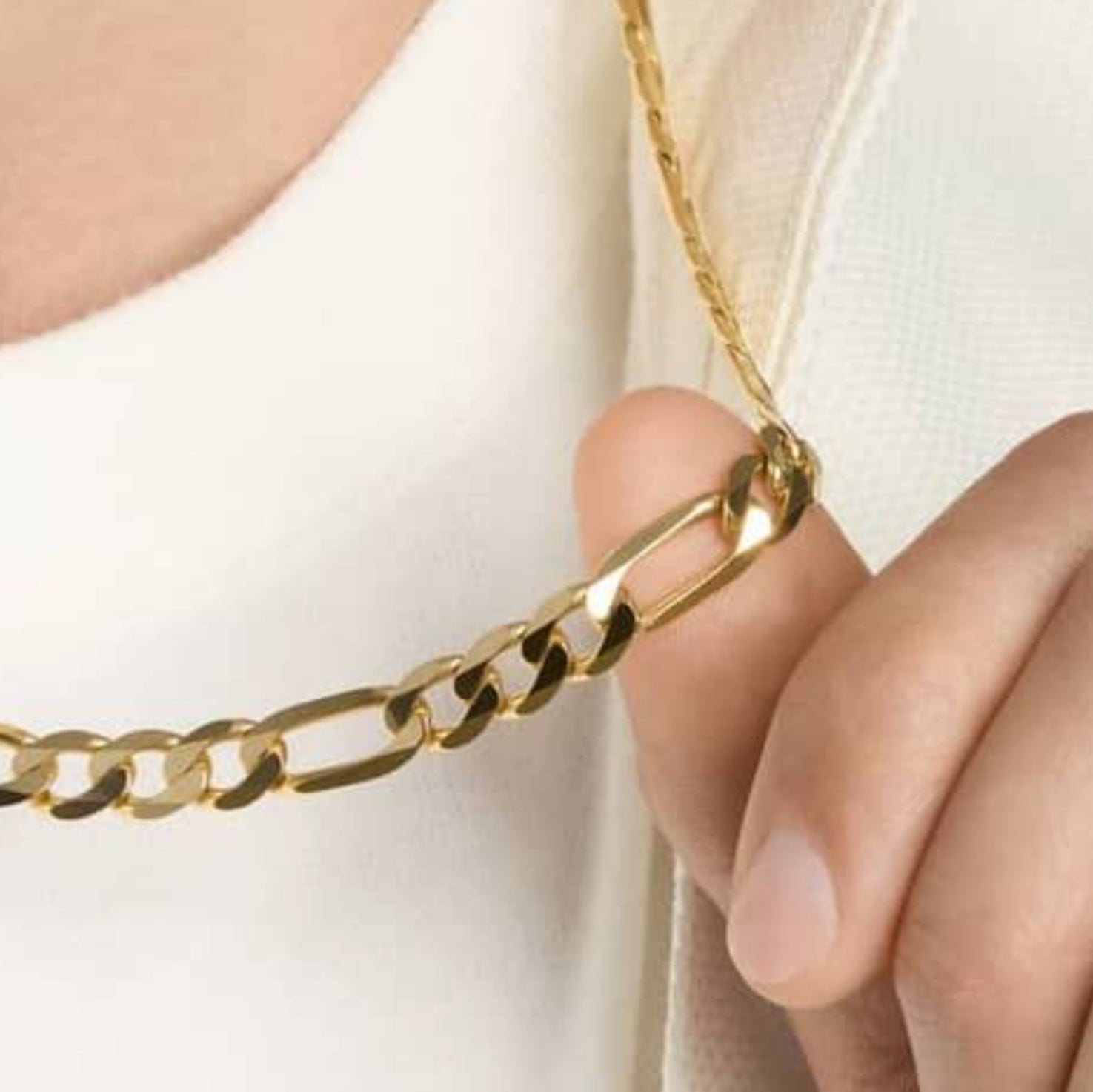 14K yellow gold Figaro chain necklace held in hand, showing lobster clasp and shine.